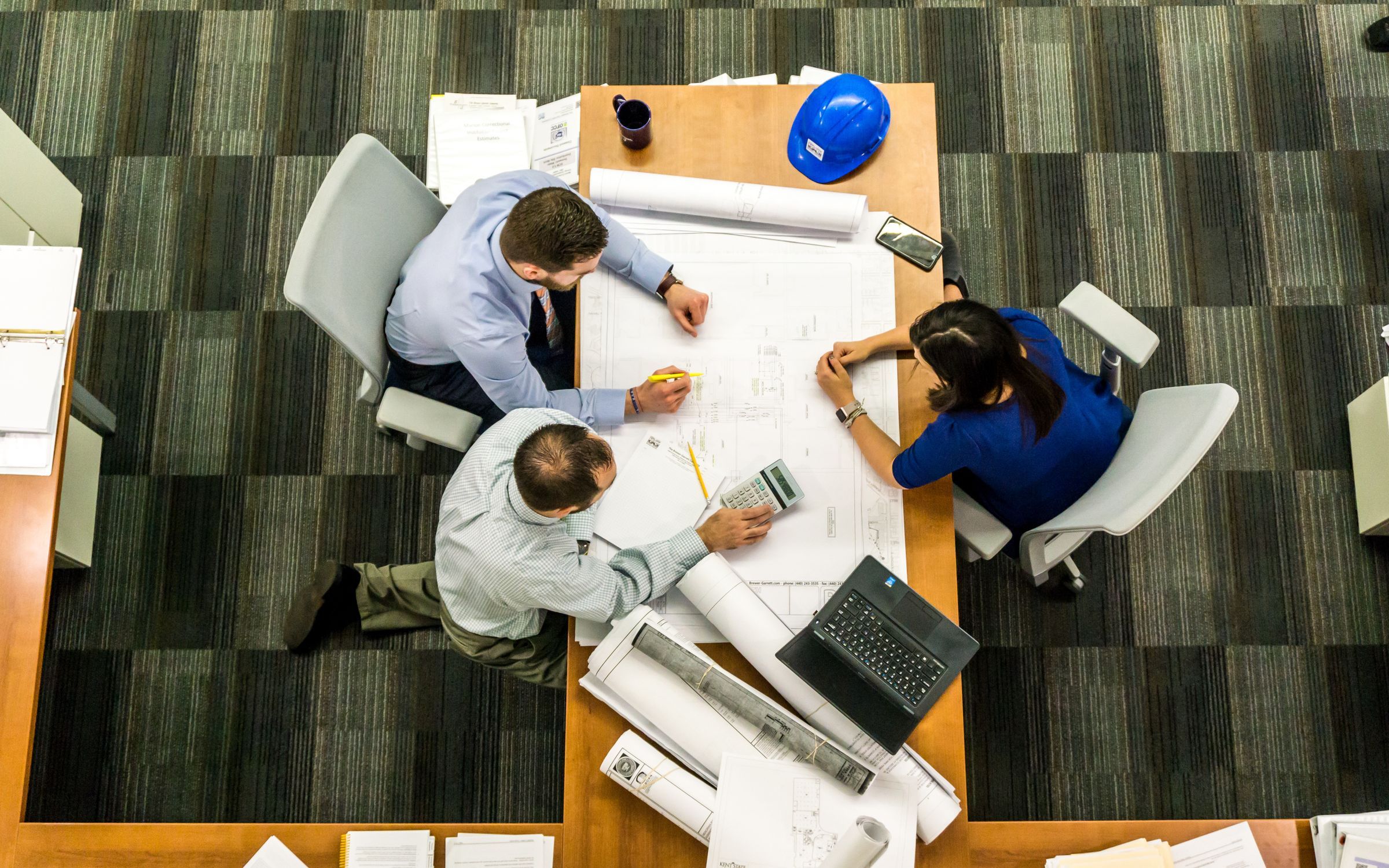 Overhead view of a project team reviewing technical drawings and a laptop around a meeting table