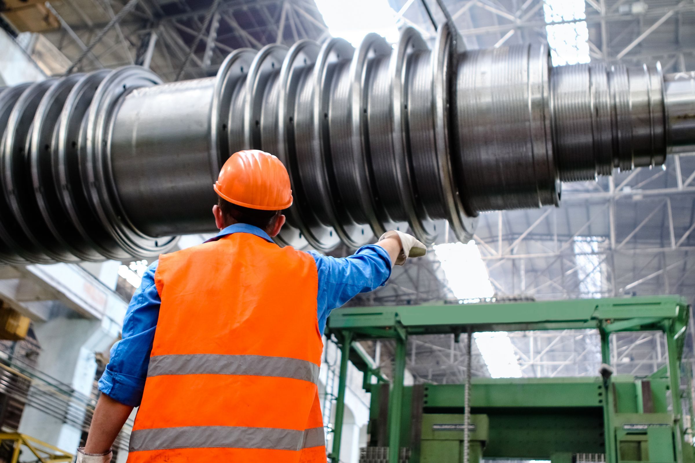 A worker in a high-visibility vest and hard hat beside heavy industrial machinery in a workshop